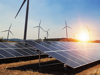 Photo of solar panels and wind turbines at sunset